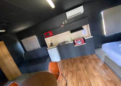 Compact cabin interior with kitchenette, small fridge, microwave, seating, and bed in Cabin 54. One of the Cabins, Dwellings, Caravans, & Glamping Tents at Stawell Grampians Gate C&C Park.