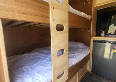 Timber interior with bunk beds and compact fridge in a retro caravan. One of the Cabins, Dwellings, Caravans, & Glamping Tents at Stawell Grampians Gate C&C Park.
