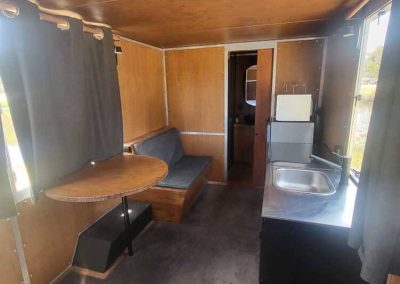 Interior of a brown caravan with seating, round dining table, and kitchenette. One of the Cabins, Dwellings, Caravans, & Glamping Tents at Stawell Grampians Gate C&C Park.