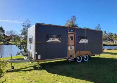 A sleek black-and-wood Hammervan nestled on the grassy waterfront, perfect for a peaceful glamping getaway. One of the Cabins, Dwellings, Caravans, & Glamping Tents at Stawell Grampians Gate C&C Park.