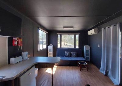 Modern cabin interior with kitchenette, couch, and large windows letting in natural light. One of the Cabins, Dwellings, Caravans, & Glamping Tents at Stawell Grampians Gate C&C Park.