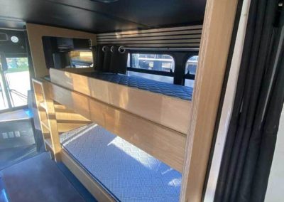 Interior of a converted bus featuring timber-framed bunk beds with windows and a skylight above. One of the Cabins, Dwellings, Caravans, & Glamping Tents at Stawell Grampians Gate C&C Park.