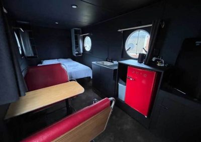 Interior of a retro caravan with round windows, a red retro-style fridge, compact dining area, and made-up double bed. One of the Cabins, Dwellings, Caravans, & Glamping Tents at Stawell Grampians Gate C&C Park.