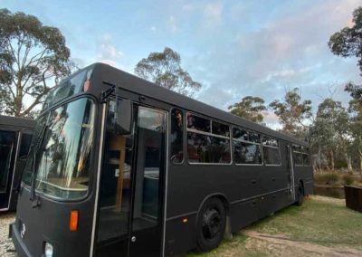 A black converted bus parked on grass, with windows along the side and an entry door open at the front. One of the Cabins, Dwellings, Caravans, & Glamping Tents at Stawell Grampians Gate C&C Park.