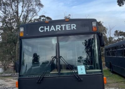 Front view of a matte black converted bus. The bus is parked on gravel and grass. One of the Cabins, Dwellings, Caravans, & Glamping Tents at Stawell Grampians Gate C&C Park.