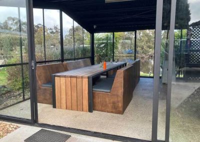 Covered outdoor dining area with built-in timber bench seating and a long table at Stawell Grampians Gate C&C Park.
