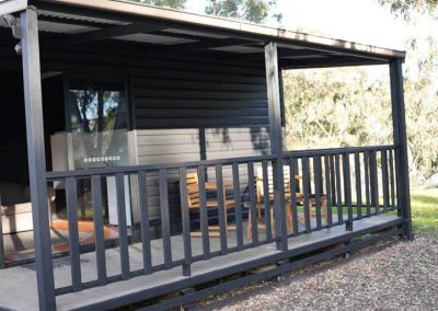 Covered timber deck with railing and outdoor dining furniture, attached to a modern black cabin at Stawell Grampians Gate C&C Park. One of the Cabins, Dwellings, Caravans, & Glamping Tents available at the park.