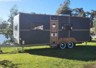 A custom-designed caravan with a retro aesthetic, parked lakeside at Stawell Grampians Gate C&C Park – one of the options among Cabins, Dwellings, Caravans, & Glamping Tents.