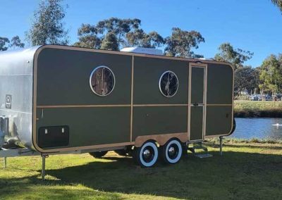 A charming Hammervan sits beside the peaceful water at Stawell Grampians Gate C&C Park. One of the Cabins, Dwellings, Caravans, & Glamping Tents at Stawell Grampians Gate C&C Park.
