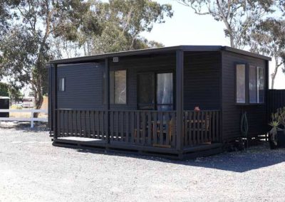 Cabin 91 is a compact and stylish dwelling featuring a veranda and sleek dark exterior, nestled in the tranquil surroundings of Stawell Grampians Gate C&C Park. One of the Cabins, Dwellings, Caravans, & Glamping Tents.