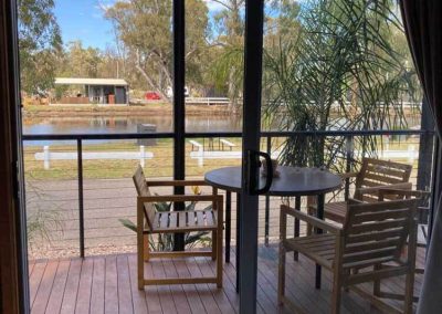 View from inside a cabin looking out onto a private deck with outdoor seating, overlooking the lake at Stawell Grampians Gate C&C Park. One of the Cabins, Dwellings, Caravans, & Glamping Tents available at the park.