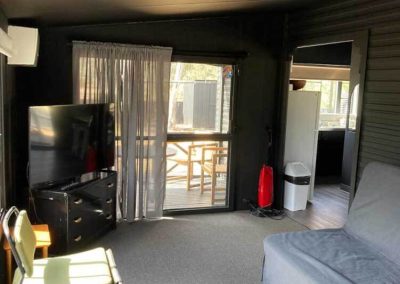 Interior of 88 showing a living space with a flat-screen TV, green chair, grey couch, and access to a private deck through a glass sliding door.