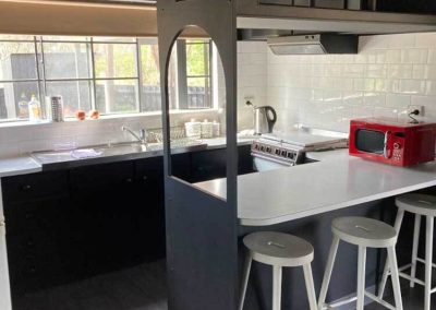 Modern kitchen inside Cabin 88 featuring a white tiled backsplash, red microwave, electric stove, black and white cabinetry, and a breakfast bar with white stools. One of the Cabins, Dwellings, Caravans, & Glamping Tents at Stawell Grampians Gate C&C Park.