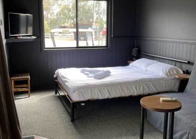 Queen bed setup with TV and window in Cabin 116. One of the Cabins, Dwellings, Caravans, & Glamping Tents at Stawell Grampians Gate C&C Park.