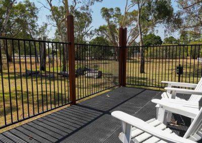 Deck with white outdoor chairs and a view across open grassy space with trees and logs. One of the options at Stawell Grampians Gate C&C Park – Cabins, Dwellings, Caravans, & Glamping Tents.