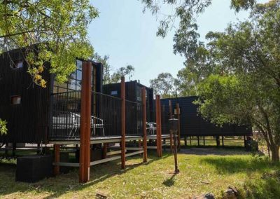 A row of elevated black cabins with large windows and private decks, surrounded by trees and greenery. One of the options available at Stawell Grampians Gate C&C Park – Cabins, Dwellings, Caravans, & Glamping Tents.