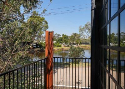 View from a balcony looking out over a small lake, with a railing in the foreground and trees, power lines, and RVs in the distance. One of the options at Stawell Grampians Gate C&C Park – Cabins, Dwellings, Caravans, & Glamping Tents.