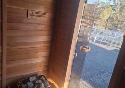 Interior view of a wooden sauna with a heater and stones, looking out to a fenced deck area at Stawell Grampians Gate C&C Park.