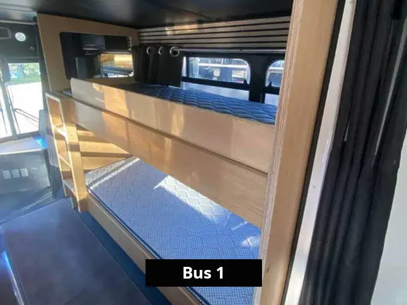 Built-in bunk beds with timber frame and privacy curtains in the front section of the bus accommodation.