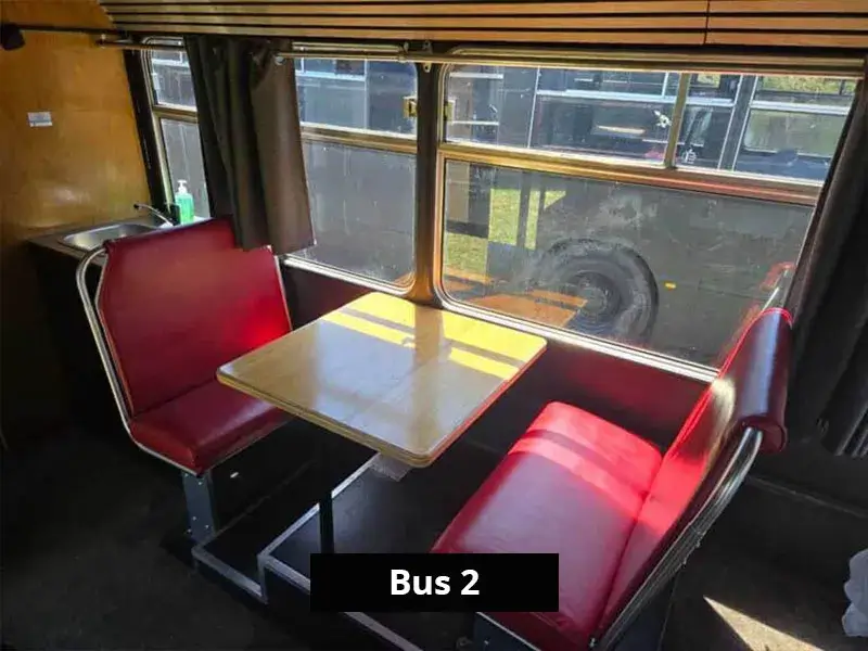 Retro red booth seating and dining table beside large windows inside the Bus 2 accommodation.