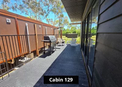 Private deck area of Cabin 129 at Stawell C&C Park, with white Adirondack chairs overlooking a grassy field surrounded by gum trees and nature, enclosed by a black steel fence.