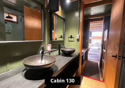 Sleek bathroom in Cabin 130 at Stawell C&C Park Grampians Gate, showcasing dual black vessel sinks, matte black fixtures, two mirrors, towel holders, and a minimalist black-and-wood interior.
