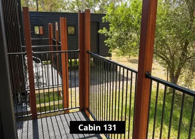 Outdoor balcony of Cabin 131 at Grampians Gate caravan park in Stawell, featuring a steel mesh floor, black railing, and timber posts, overlooking greenery and nearby cabin units.