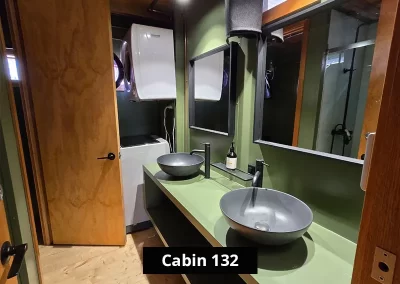Modern bathroom in Cabin 132 at Grampians Gate caravan park, equipped with double matte black vessel sinks, minimalist black fixtures, wall-mounted mirrors, and a washing machine under natural light from a small window.