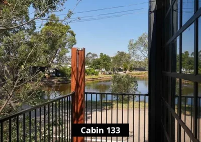 Balcony view from Cabin 133 at Staawell C&C Park Grampians Gate, overlooking a tranquil lake surrounded by trees and greenery, with a black railing and timber posts framing the water view.