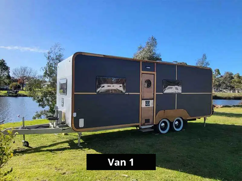 Modern caravan exterior with dual axle, dark paneling, timber trim and lakeside setting