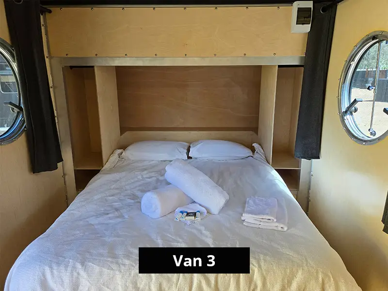 Van interior with double bed, built-in shelving, round windows and fresh linen