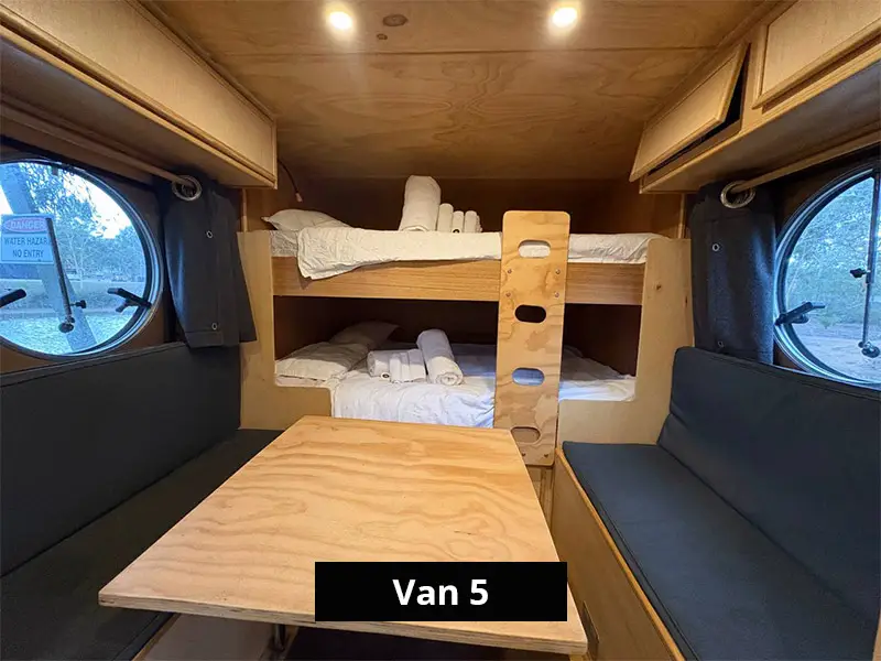 Campervan interior with timber table, bench seating, round windows and double bunk beds