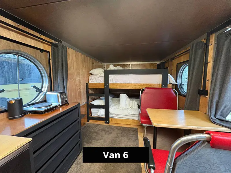 Van interior with bunk beds, dining table, red chairs, timber walls and round windows