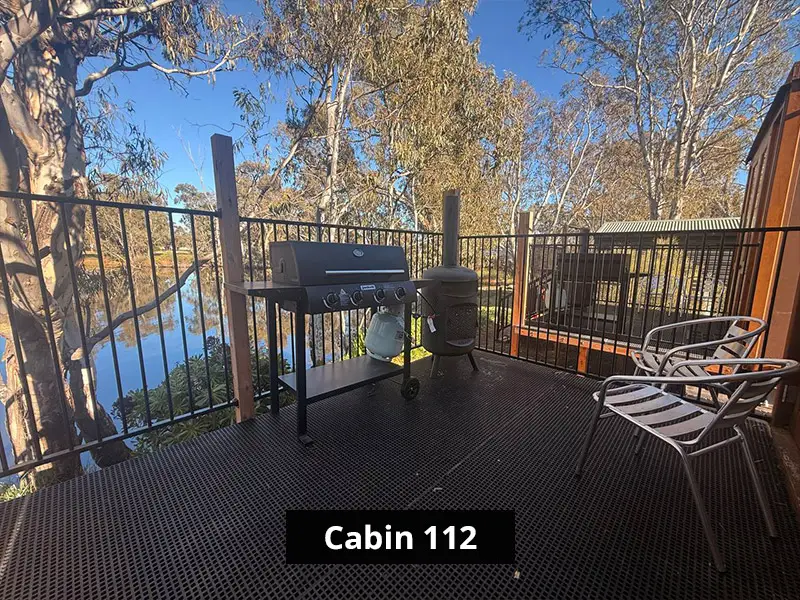 Cabin 112 exterior with glass doors, private deck seating, barbecue grill, and surrounding trees.